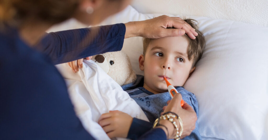 Mother takes temperature of sick boy lying in bed.